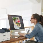 Een vrouw zit aan een bureau, gefocust op haar werk, met een Xerox® C320 kleurenprinter