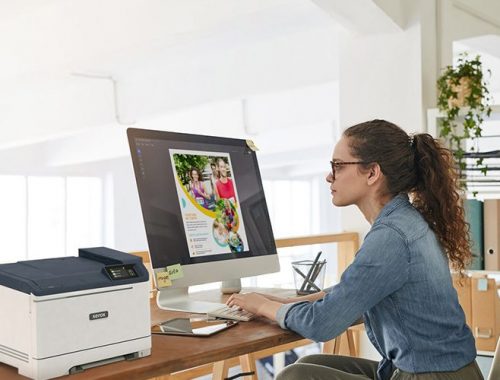 Een vrouw zit aan een bureau, gefocust op haar werk, met een Xerox® C320 kleurenprinter